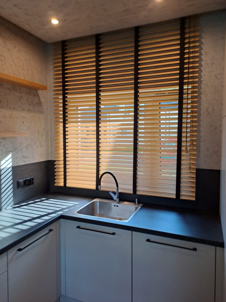 szafkami, czarnym blatem i zlewem pod oknem.